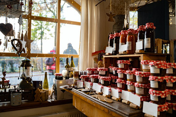 Glass jars with large variety of natural homemade country jams and honey on counter of cozy shop with Christmas decorations on November or January day in Dresden, Germany. Food, holidays, celebrations