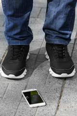 Legs of man and damaged mobile phone on pavement outdoors, closeup