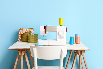 Tailor's workplace with sewing machine and threads near blue wall