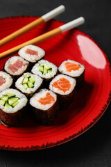 Plate with delicious maki rolls and wooden chopsticks on dark background, closeup