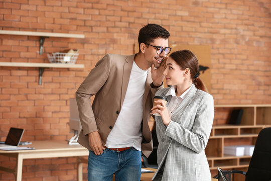 Young Man Sharing Gossip With His Colleague In Office