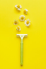 Safety razor and chamomile flowers on yellow background