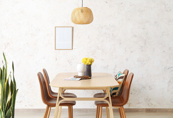 Dining table with flowers in vase and chairs near light wall