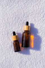 Two amber glass dropper bottles with bamboo lid against the background of a white towel. Skincare sunscreen cosmetic. Beauty concept for face body care