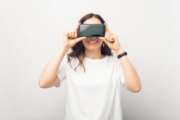 Smiling girl is covering her eyes with the phone she is holding.