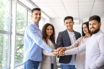 Young business colleagues putting hands together in office