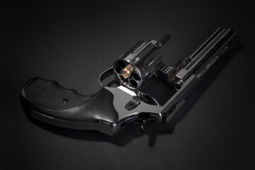 revolver gun and one bullet on black background