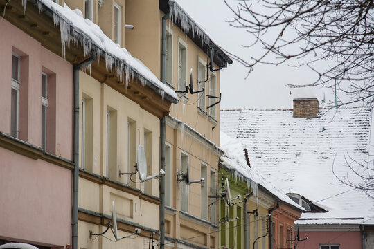 Architektura miejska zimą &ndash; ulica przedwojennych budynk&oacute;w pokryta białym puchem pod pochmurnym niebem zimowe zagrożenie - zwisające z rynien lodowe sople