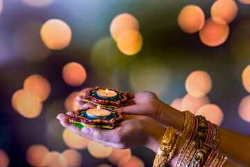 Happy Diwali - Woman hands with henna holding lit candle isolated on dark background. Clay Diya lamps lit during Dipavali, Hindu festival of lights celebration.