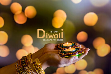 Happy Diwali - Woman hands with henna holding lit candle isolated on dark background. Clay Diya...