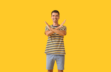 Handsome young man in stylish t-shirt showing STOP gesture on color background