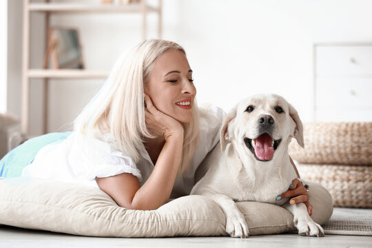 Mature woman with cute Labrador dog lying on pet bed at home