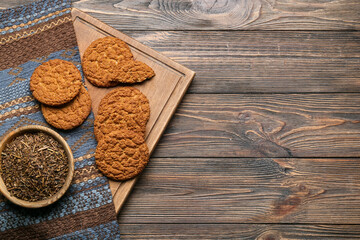 Board with tasty hojicha cookies and dry leaves on wooden background