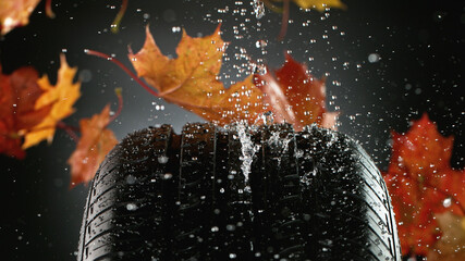 Car tire with falling autumn leaves and splashing water