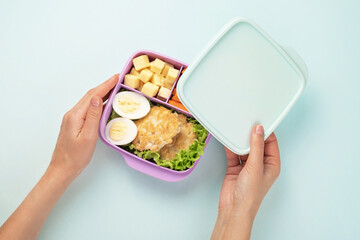 Woman opens a plastic lunch box with lunch. Blue background