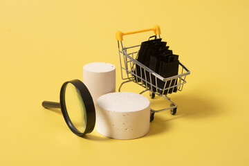 Empty mock podiums or pedestals and miniature supermarket cart with shopping bags in black friday sale on yellow background