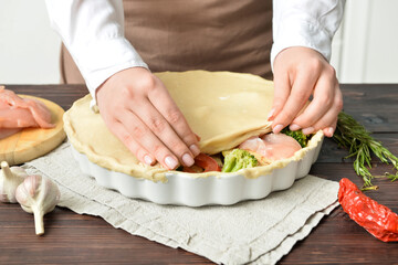Woman preparing chicken pot pie with vegetables at kitchen table, closeup