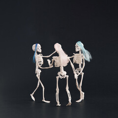 Three skeletons like three graces dancing on a black background. Square crop. Halloween motif with...