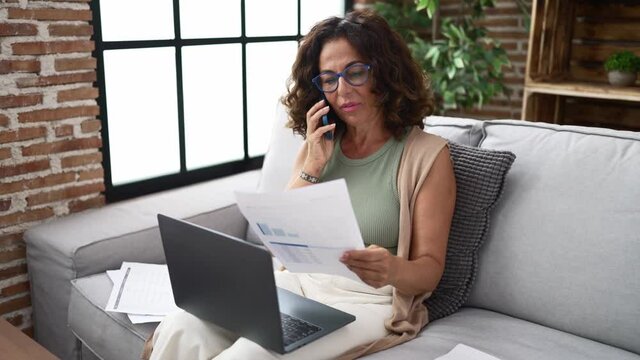 Middle age hispanic woman doing countability with documents and laptop