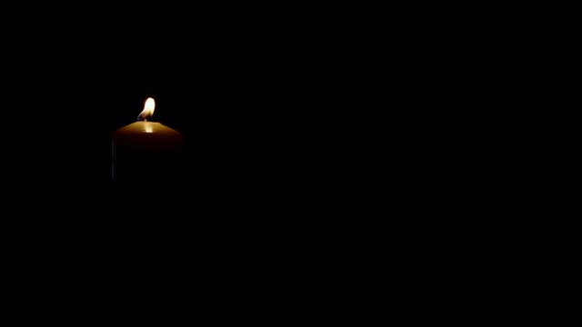Burning candle isolated on black background flame moving in wind left side of picture shot in 4k super slow motion