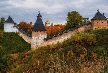 Powerful defensive walls and beautiful churches on the hills in the Dormition Pskovo Pechersky Monastery in the city of Pechery, Pskov Region, Russia during the golden autumn - obrazy, fototapety, plakaty