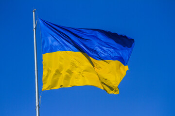 Flag of Ukraine waving in the wind on flagpole against the background of a clear sky on sunny day, close-up