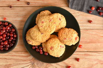 Plate with fresh cranberry cookies and berries on wooden background