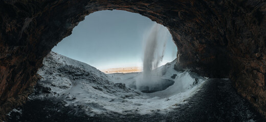 View of Seljalandsfoss waterfall at dawn in winter in Iceland with snow and frozen ice in the foreground.