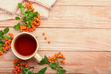 Cup of hot tea and rowan berries on wooden background