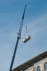 Crane lifts the container to the roof of building under construction. Crane against blue sky.