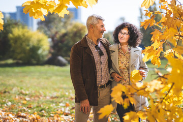 A mature couple, embracing, communicates under a tree in an autumn park. Portrait of a mature couple 50 years old in an autumn park.