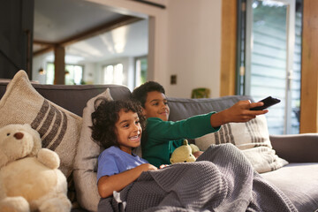 Two cheerful boys watching TV using remote control
