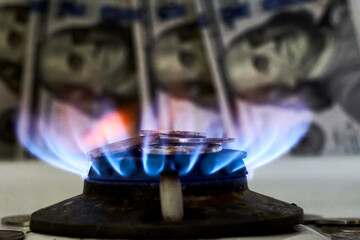 Burning gas stove burner and US dollar banknotes. Pay for natural gas, gas bill, tariff. Pile of coins and burning fire gas stove hob and money
