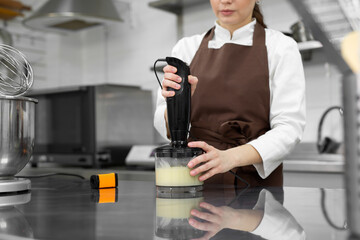 Female pastry chef prepares a mirror icing for a cake, whips it in a blender.