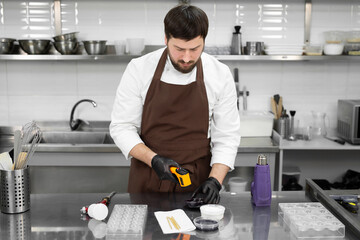 Male pastry chef measures the temperature of the chocolate glaze with a non-contact thermometer in...