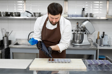 Chocolatier pours the chocolate into the molds. Pastry bag chef fills the hot melted chocolate into a silicone mold.