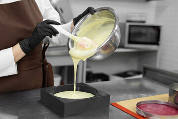 Young female pastry chef pours liquid mousse into a mold. Preparation of cake, dessert in a professional kitchen. - obrazy, fototapety, plakaty