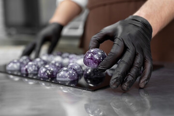 Close-up of the hand of a male pastry chef-a man laying out colored chocolates on a black mirror...