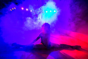 Attractive young sexy female dancer sitting in the splits near the pole.
