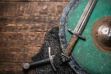Knight sword, shield and armor on the wooden flat lay background with copy space.