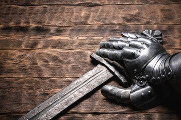 Knight sword and steel gloves on the wooden table close up background with copy space.
