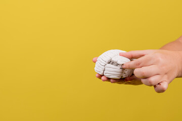 manos de una persona con un cerebro roto en fondo amarillo - obrazy, fototapety, plakaty
