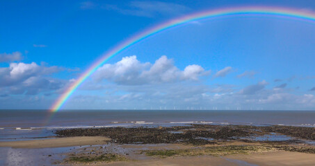 under a beautful rainbow, distant wind turbines in action at Gwynt y Môr (Sea wind) 576-megawatt offshore electricity generating wind farm with 160 x 150m high turbines in Colwyn Bay Wales