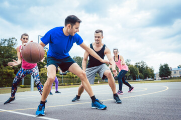 Group of happy young people playing basketball on outdoor court