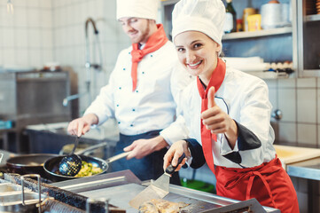 Chefs in restaurant kitchen cooking and giving the thumbs up as a sign of recommendation