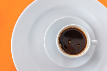 Black hot and fragrant coffee in a mug on a saucer on a bright orange table in the cafeteria