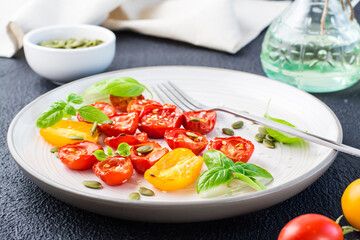 Ready-to-eat vegetarian food. Dried tomatoes with basil, sesame seeds and pumpkin on a plate on a black background