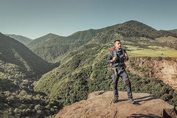 Fototapeta premium A male traveler with a trekking backpack climbs a rock in the mountains. Long distance trails and hike concept