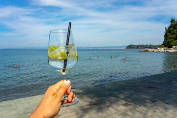 woman drinking a gin tonic on the beach in Slovenia next to the mediterranean sea