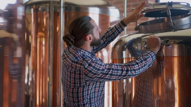 Concentrated engineer repairing large beer tank in brewery. Side view portrait of focused professional male Caucasian expert fixing broken equipment indoors. Alcohol production and maintenance